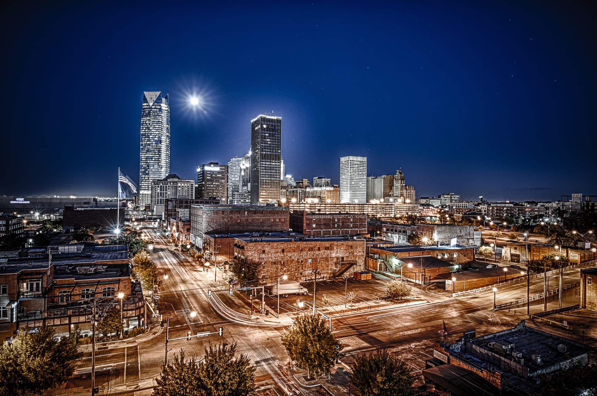 Bricktown warehouse district in Oklahoma City at night, with the downtown skyline behind it.