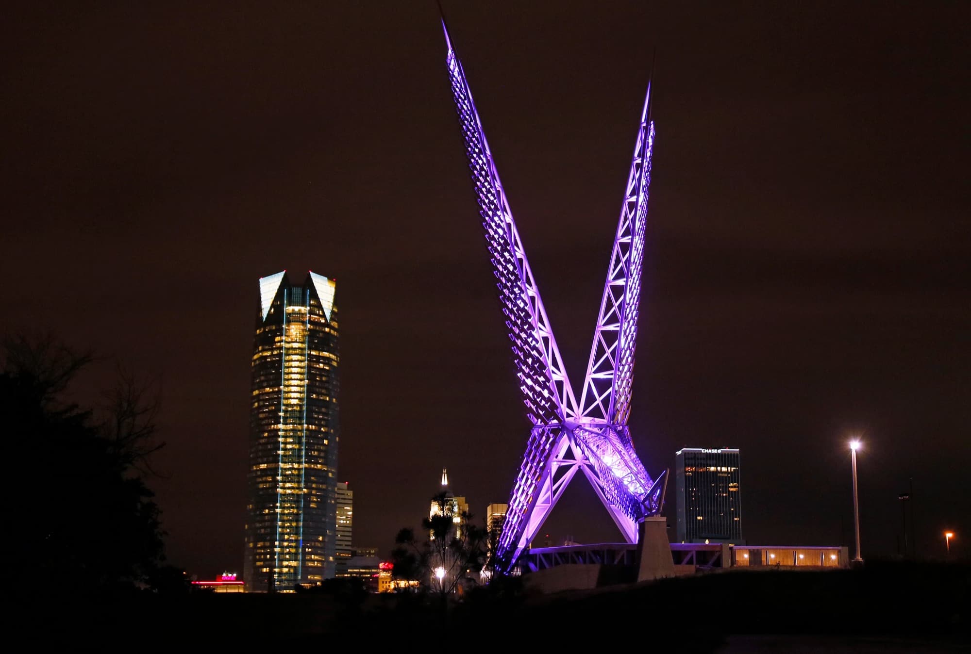 The Skydance pedestrian bridge lit at night with the Oklahoma City skyline behind it.